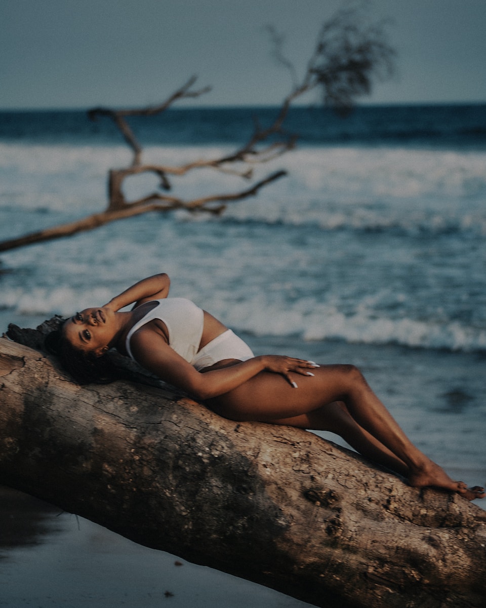 a woman laying on top of a tree branch next to the ocean