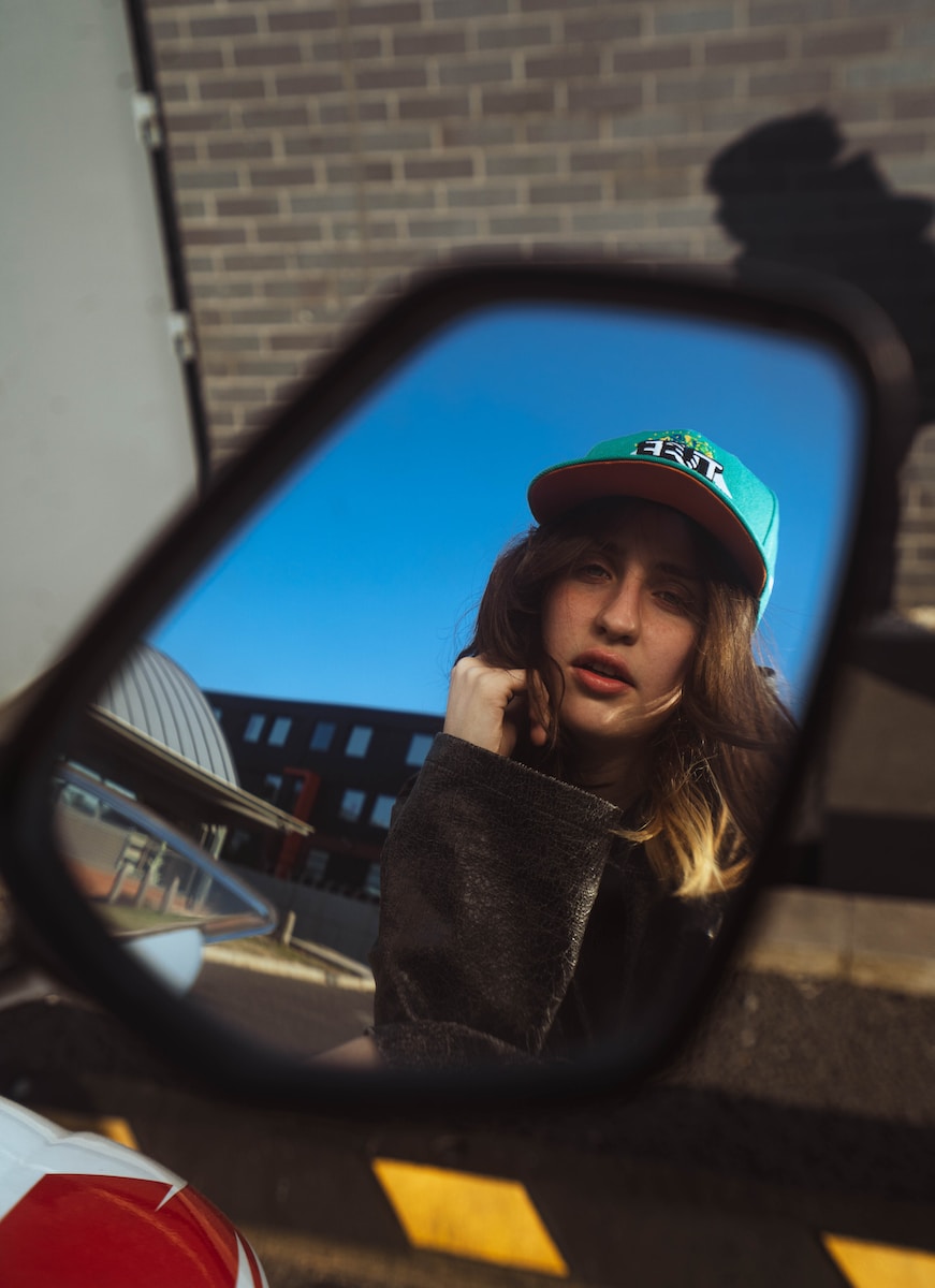 a woman in a cap is reflected in a rear view mirror
